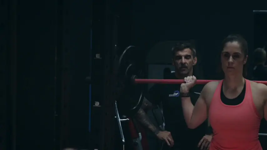 A coach spotting a member under a barbell in the rack