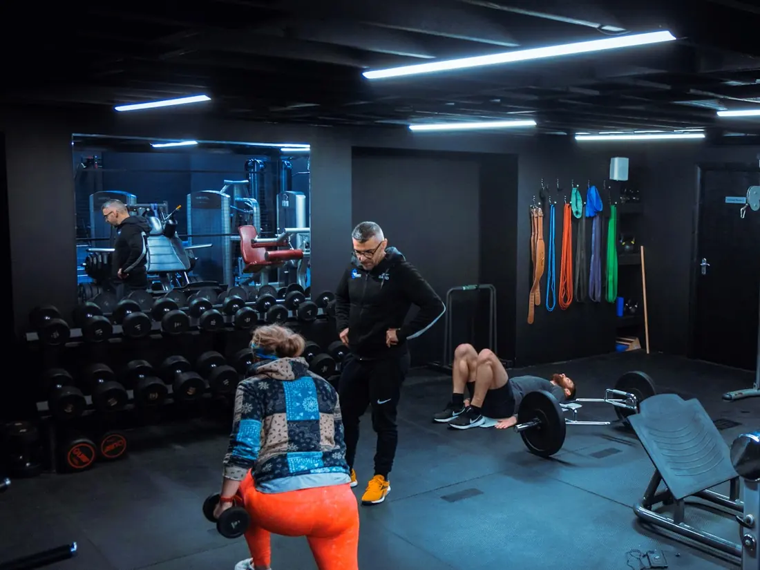 A coach working with two members on the gym floor at BodyMechanics